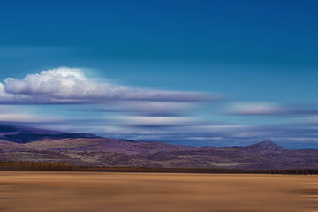 panoramic view of plain at root of snow-covered mountains on blue sky background
