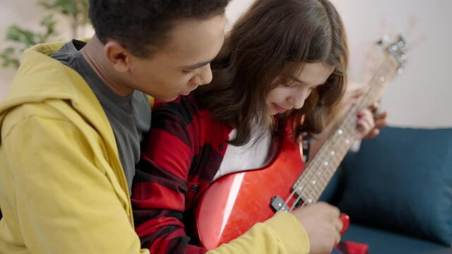 Teenage guy teaching girlfriend to play the guitar, learning chords, hobby