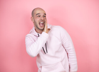 Young bald man wearing casual sweatshirt over pink isolated background hand on mouth telling secret rumor, whispering malicious talk conversation