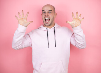 Young bald man wearing casual sweatshirt over pink isolated background showing and pointing up with fingers number ten while smiling confident and happy