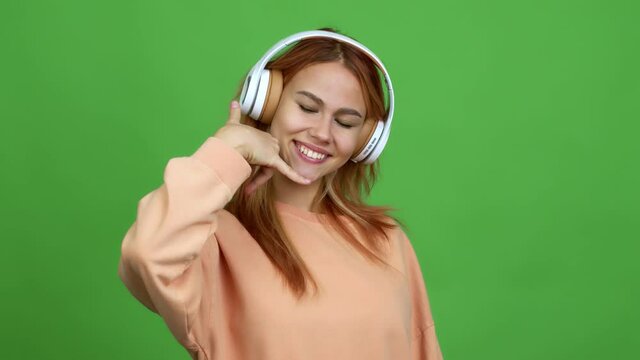 Teenager girl listening music with headphones making phone gesture and speaking with someone. Call me back sign over isolated background