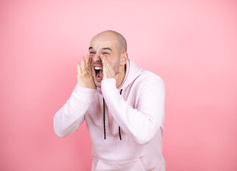 Young bald man wearing casual sweatshirt over pink isolated background shouting and screaming loud to side with hands on mouth