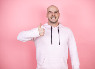 Young bald man wearing casual sweatshirt over pink isolated background smiling and doing the ok signal with his thumbs