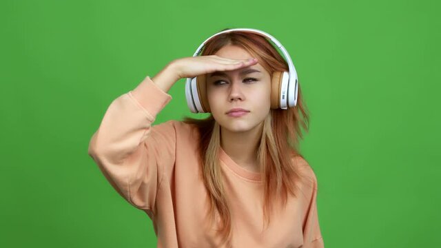 Teenager girl listening music with headphones looking far away with hand to look something over isolated background