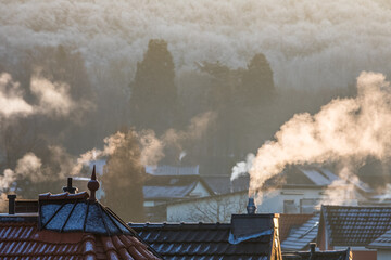 Rauchende Schornsteine über den Häuserdächern im Winter, angestrahlt von der Sonne