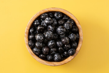 Fresh blueberries in wooden bowl on yellow background. Top view