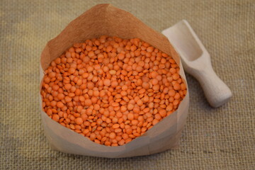 Red lentil in paper bag on jute fabric background wooden spoon blurred