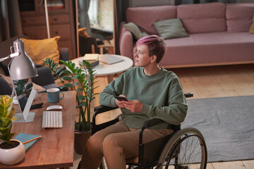Young woman with short hair sitting in wheelchair in front of her workplace and using her mobile phone - obrazy, fototapety, plakaty
