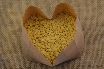 Yellow lentil in paper bag heart shaped on jute fabric background