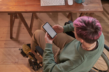 High angle view of disabled woman with short hair sitting on wheelchair and working on her mobile...