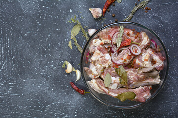 Pork ribs, sliced and marinated with onions. Shish Kebab meat in a glass bowl and spices on a textured background.Selective focus, close-up, top view.Homemade food.