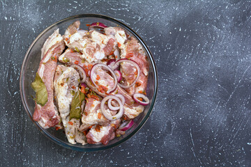 Pork ribs, sliced and marinated with onions. Shish Kebab meat in a glass bowl and spices on a textured background.Selective focus, close-up, top view.Homemade food.