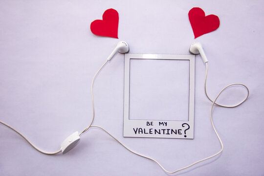 concept love music lovers earphones with red hearts coming out with a picture frame with words be my valentine flat lay on white background