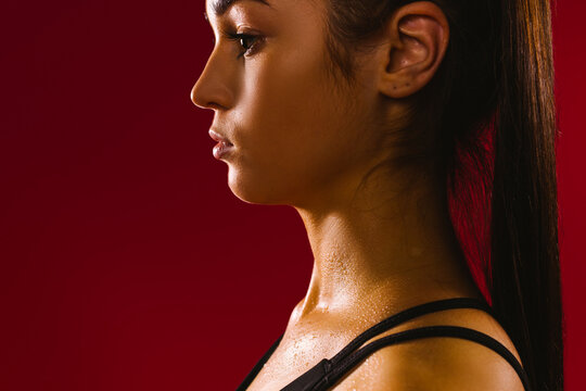 An enlarged profile photo of a caucasian girl sweating after physical exertion against a red background. Dark photo of real brunette woman