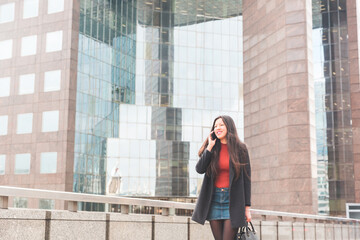 Beautiful Chinese business woman walking in London and talking on the phone - Young Asian girl wearing smart casual clothes with a denim skirt and grey coat - Young entrepreneur in the city