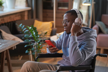 African man in headphones using his mobile phone while resting at home