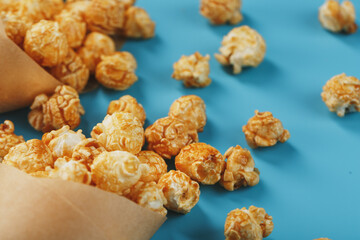 Popcorn in caramel glaze in a paper envelope on a blue background.