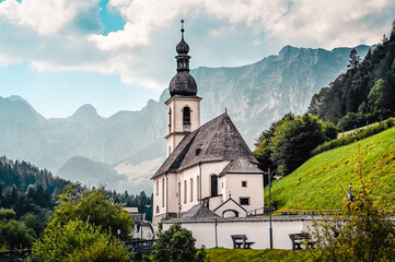 Fototapeta premium Amazing alpine landscape in the Bavarian Alps with the church of St. Sebastian in the national park Berchtesgaden. The church is standing in a valley surrounded by forested hills and rough mountains.