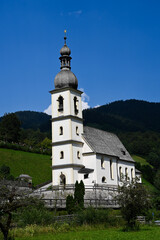 The church of St. Sebastian in the national park Berchtesgaden, Bavaria, Germany. The church is standing in a valley surrounded by forested hills.
