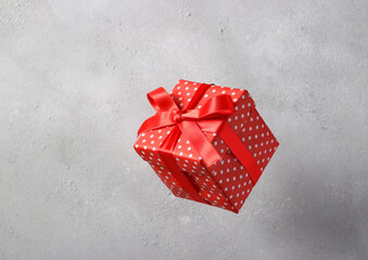 Gift box in red paper with a red ribbon flies on a light gray background. Valentine's Day Concept, Birthday, Mother's Day