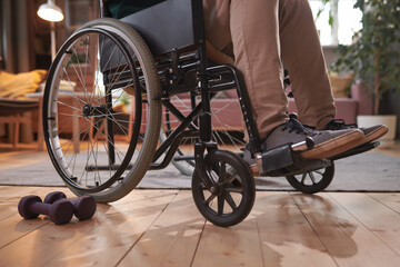 Obraz premium Close-up of man sitting in wheelchair and exercising with dumbbells at home