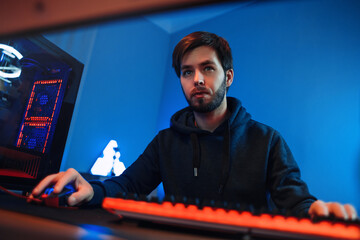 Portrait of professional young gamer playing online on his modern PC. He is serious and focused on game, having esport tournament, playing in a multiplayer video game at home. First-Person Shooter