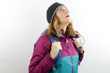 Young woman hiker with wool cap and backpack looking amazed upwards.