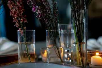 Genista and bergrass in a glass vase on a table set for a festive dinner.