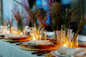 Decorated table ready for dinner. Beautifully decorated table set with flowers, candles, plates and serviettes for wedding or another event in the restaurant. Red and rose flowers on grass.