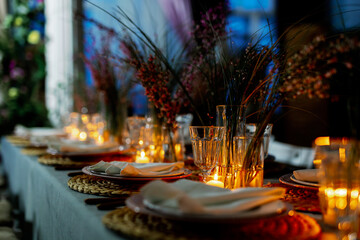 Table decorated with genista flowers and bergrass. Serving with wicker coasters for plates, napkins, burning candles and glasses. Decorations and table for wedding and dinner parties.