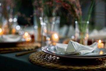 Table decorated with genista flowers and bergrass. Serving with wicker coasters for plates, napkins, burning candles and glasses. Decorations and table for wedding and dinner parties.