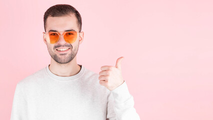 Bearded shows sign super with fingers, man in love wears glasses in the shape of a heart, portrait, pink background with copyspace