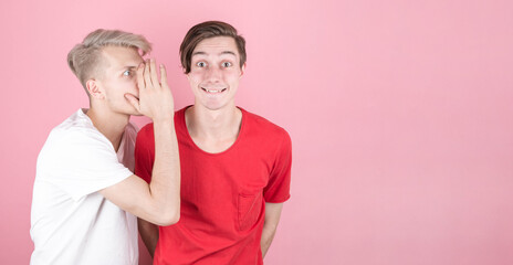 Close-up portrait of two young people, one whispering secrets to the other, shocked and very surprised, with their mouths wide open, isolated on a pink background.  with copyspace