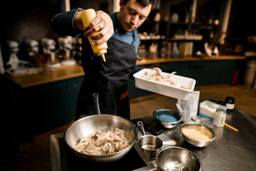 high angle view of chef who pours sauce on mushrooms in fried pan