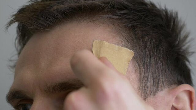 Injured man head with dry blood. Medical Treatment of wounds. Close-up. Take off antiseptic band-aid plaster.