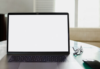Laptop open with white blank screen on a glass table at a home office workspace with blurred bright...