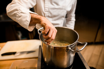 close-up on the hand of male chef who is stirring soup in pot with spoon