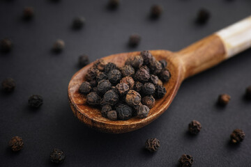 Organic whole black peppercorns in a wooden spoon. Low key. Close up. 