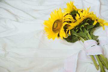 Candid authentic Yellow sunflowers bouquet on fabric white background. Background with bouquet of yellow sunflowers on white bed sheet. Sunny Days, Summer floral concept