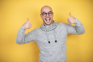 Naklejka premium Young bald man wearing glasses over yellow background smiling and doing the ok signal with his thumbs