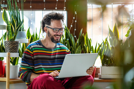 Young Man Working At Home With Laptop Surrounded By Houseplants