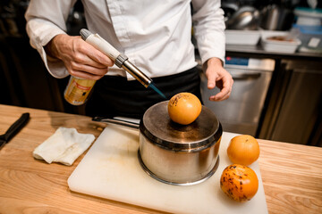male chef gently burns yellow tomatoes with burner in the kitchen