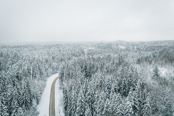Mesmerizing aerial view of a beautiful road surrounded by snow-covered fir trees, snow storm