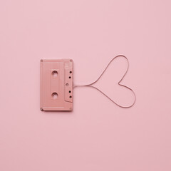 Pink audio cassette tape on pastel background. Film shaping heart. Love valentines concept.