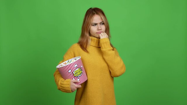 Teenager girl holding a bowl of popcorns having doubts while scratching head over isolated background