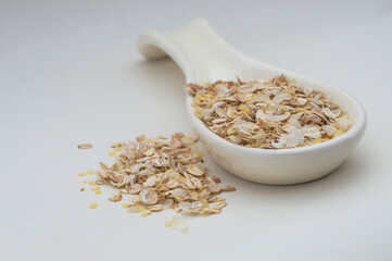 Ceramic white spoon with flakes of various cereals on a white background.