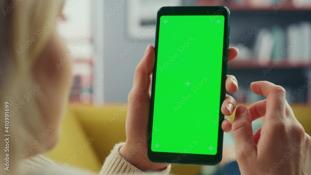 Aufkleber Beautiful Authentic Female Using a Smartphone with Green Screen Mock Up Display at Home Living Room while Lying on a Couch Sofa. She's Browsing the Internet and Checking Videos on Social Networks.