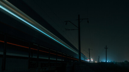 Fototapeta na wymiar A train shot in motion at night. The train moves on the railroad into the distance. Blurred train.