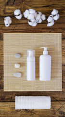 Fototapeta na wymiar Flat lay with cosmetics bottles, towel, stones and a branch of cotton on wooden background. Natural, organic beauty product concept. Spa, cosmetics flat lay in oriental stile. Bath home procedure