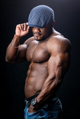 Shirtless muscular unrecognizible man in cap. Bodybuilder half turned to the camera poses. Black studio backgound.